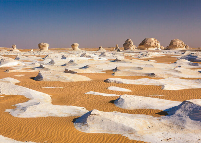 Las rocas blancas del Desierto Blanco, bañadas por los tonos cálidos y vibrantes de un amanecer o atardecer espectacular, con sombras alargadas