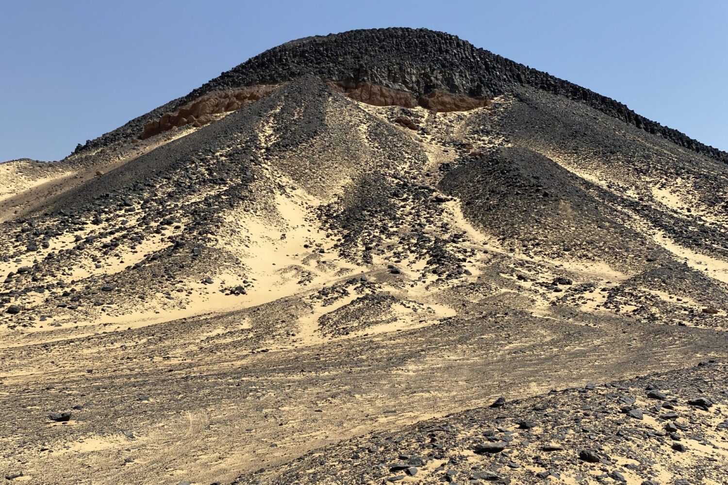 Deserto Negro: Onde Rochas se Erguem como Picos Vulcânicos Grandes formações rochosas escuras e cónicas, semelhantes a pequenas montanhas, compostas de pedras vulcânicas pretas no Deserto Negro do Egito