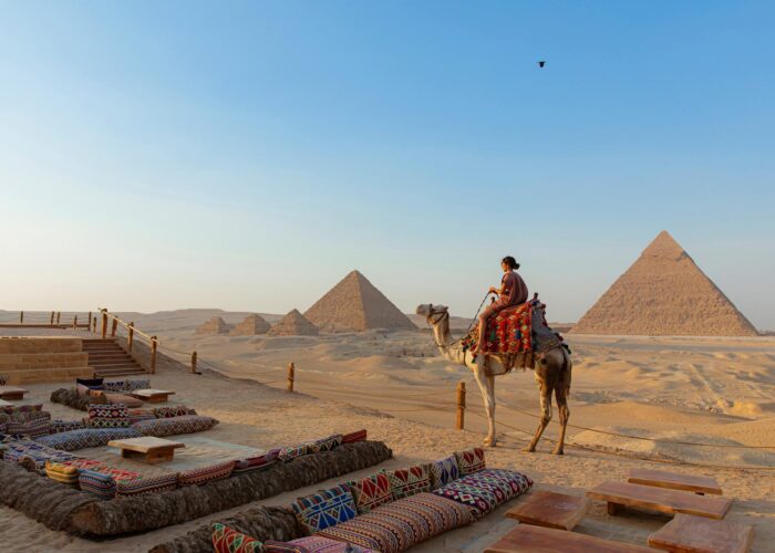 A traditional Bedouin dinner setup in the desert, with low tables and rugs, illuminated by lanterns and the majestically lit Giza Pyramids in the background