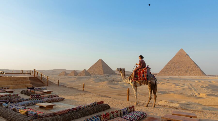 A traditional Bedouin dinner setup in the desert, with low tables and rugs, illuminated by lanterns and the majestically lit Giza Pyramids in the background