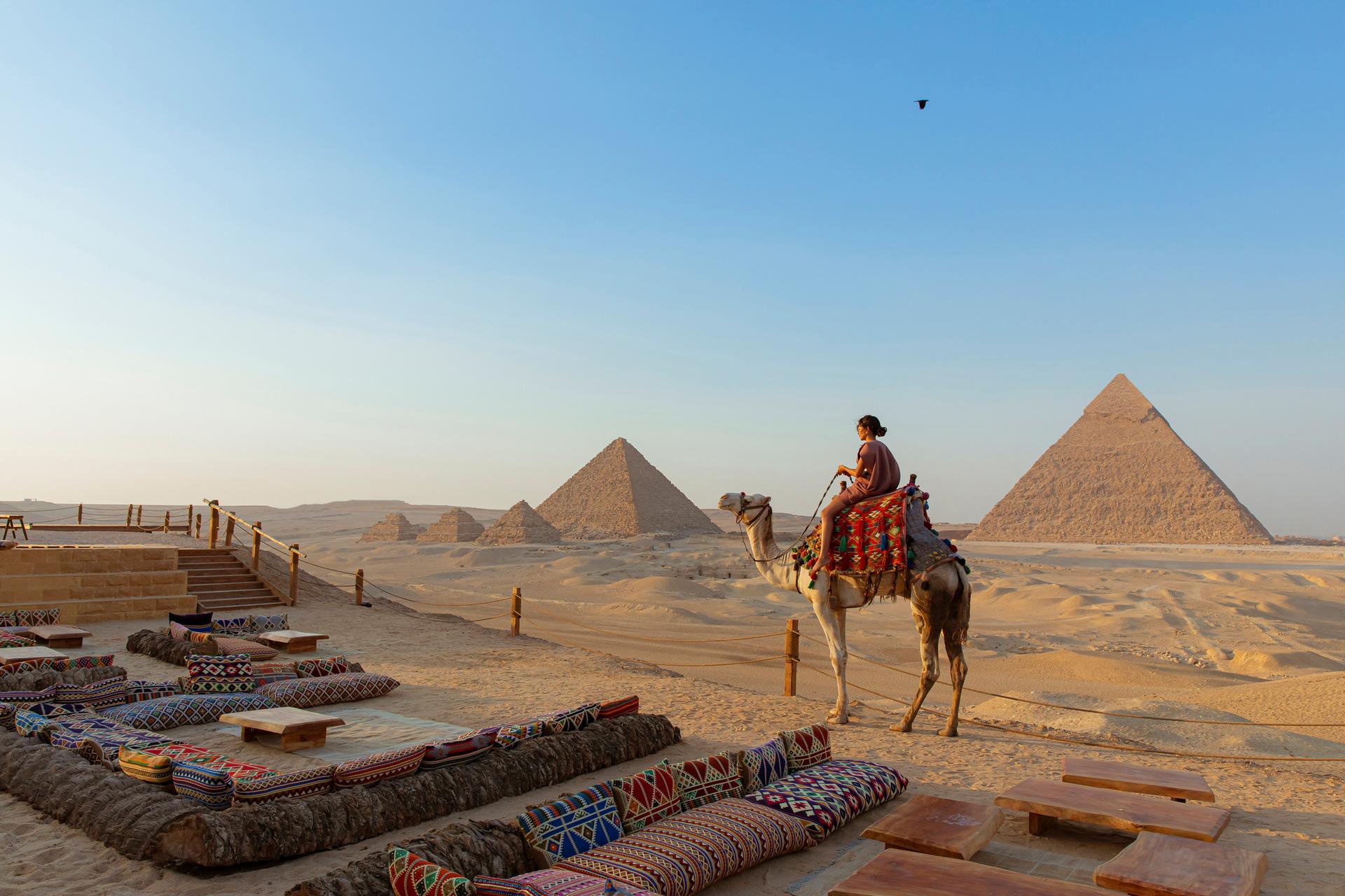 A traditional Bedouin dinner setup in the desert, with low tables and rugs, illuminated by lanterns and the majestically lit Giza Pyramids in the background