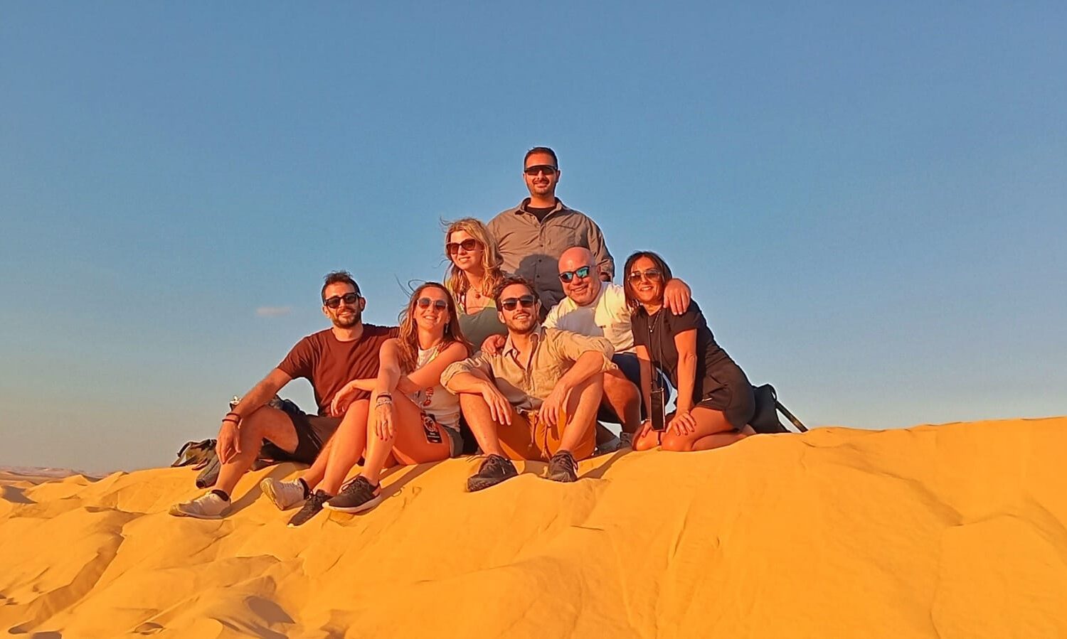Siwa: Belleza del Desierto en Buena Compañía Un grupo de amigos contemplando el vasto y hermoso paisaje del desierto de Siwa al atardecer, con dunas doradas bajo un cielo colorido