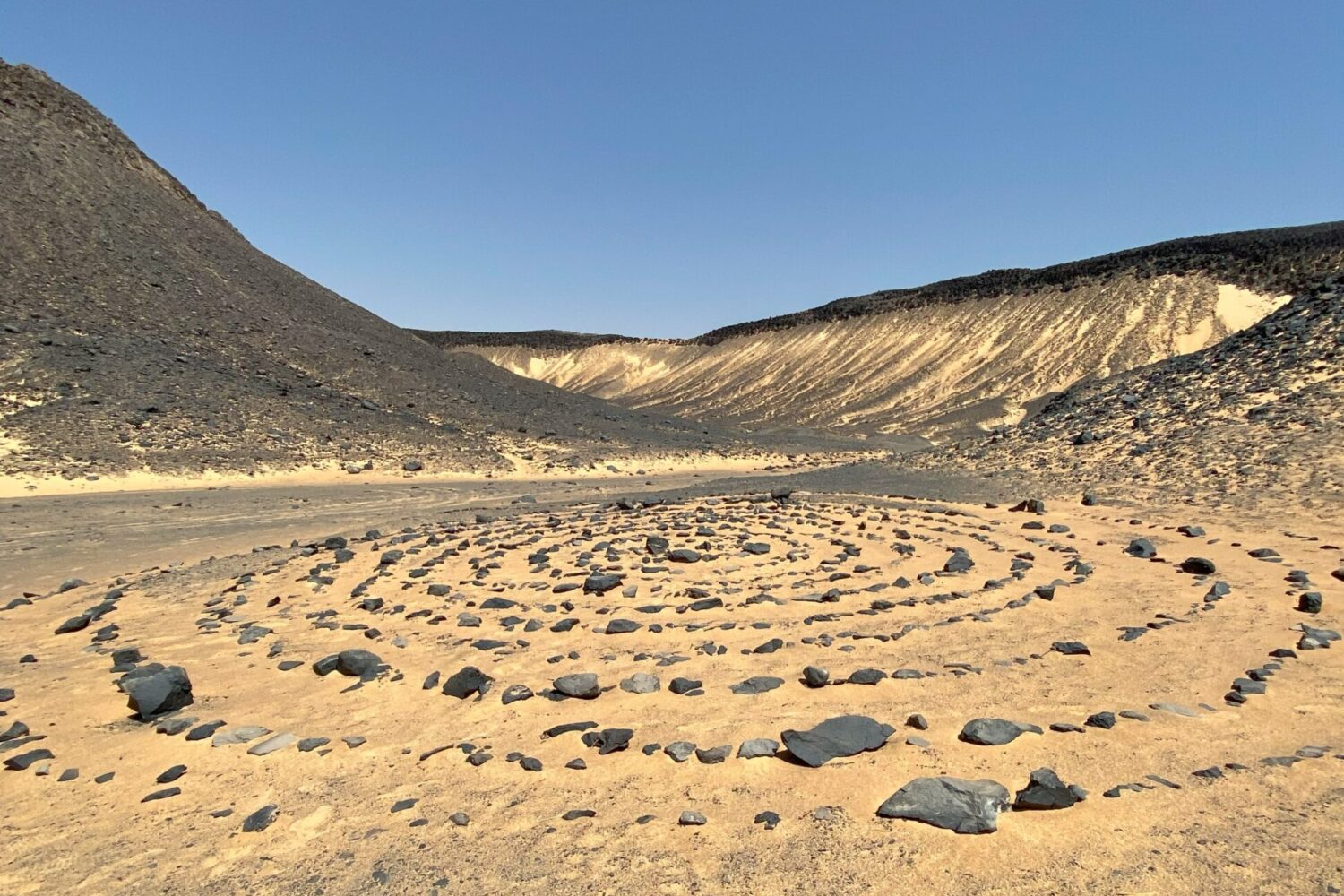 Des collines et formations rocheuses sombres et coniques, recouvertes de pierres volcaniques noires, s'étendant dans le Désert Noir en Égypte