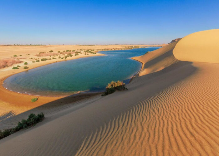 Vue panoramique du Lac Magique au Fayoum, avec ses eaux aux couleurs changeantes, entouré de dunes de sable et d'un ciel clair