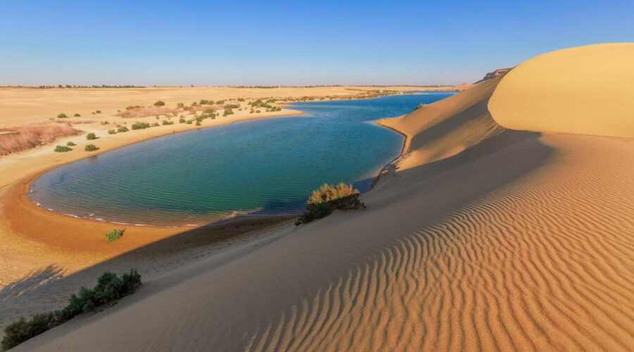 The serene waters of Magic Lake in Fayoum Oasis, showcasing its characteristic color changes from blue to green throughout the day, surrounded by desert dunes
