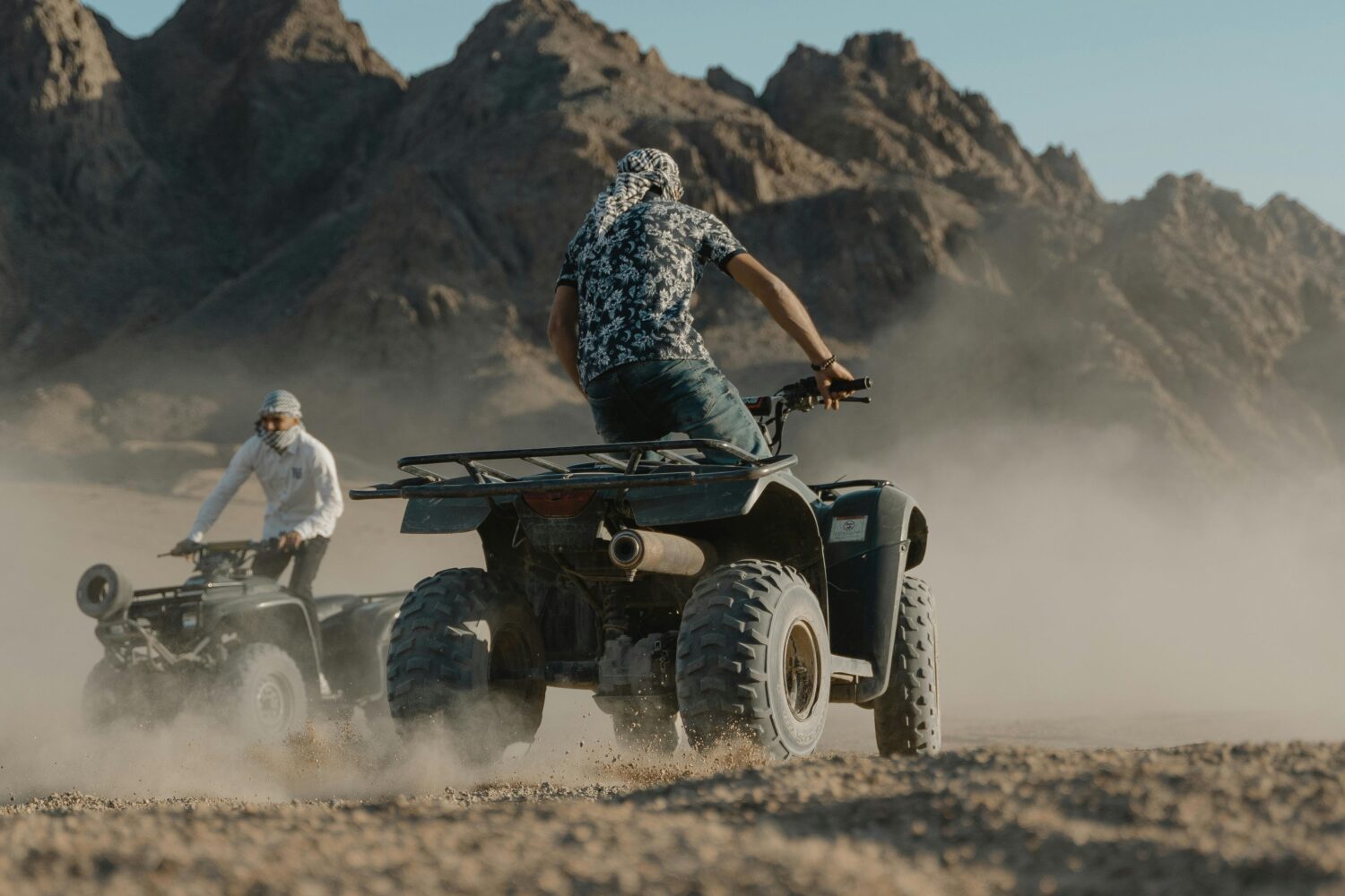 Deux amis souriants conduisent un buggy à travers un paysage désertique, soulevant un nuage de poussière derrière eux