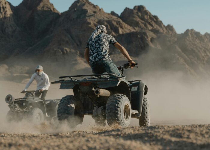 Deux amis souriants conduisent un buggy à travers un paysage désertique, soulevant un nuage de poussière derrière eux