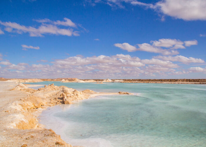 A calm Siwa salt lake reflecting the clear blue sky and distant desert, creating a surreal, mirrored landscape