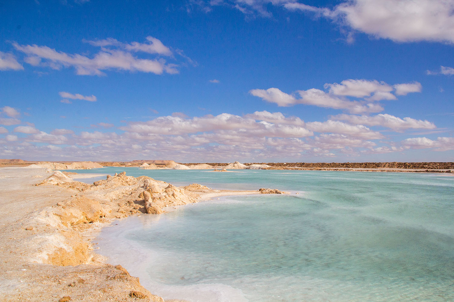 A calm Siwa salt lake reflecting the clear blue sky and distant desert, creating a surreal, mirrored landscape